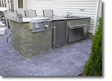 A fully equipped kitchen with a sink, grill, refrigerator, and cabinet space.